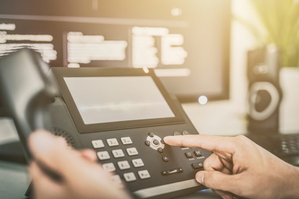 best voip systems services dialing on voip phone office computer monitor in the background